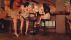 Femmes assises dans un bar nocturne, flou artistique évoquant le travail du sexe et le regard social